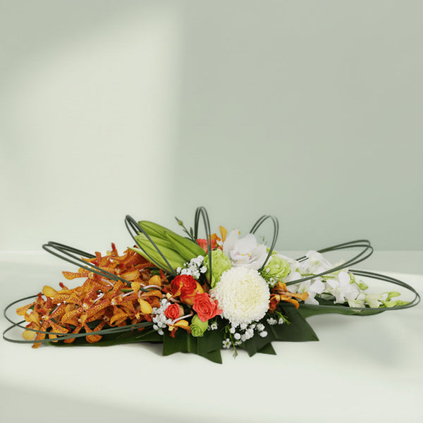 Orange orchids, white chrysanthemums and roses arranged with curved greenery on a long green tray
