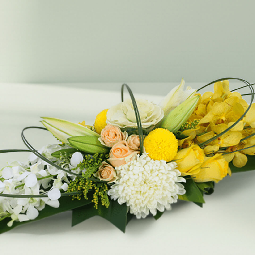 Yellow orchids, cream roses and white chrysanthemums arranged with curved greenery on a long green tray