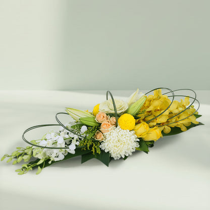 Yellow orchids, cream roses and white chrysanthemums arranged with curved greenery on a long green tray