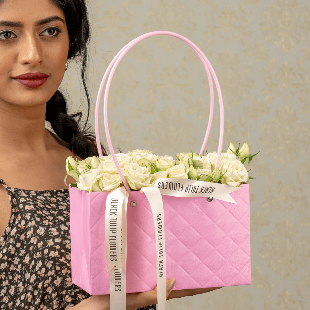 White spray roses arranged in a quilted pink flower bag with ribbon handles