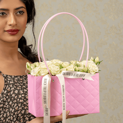 White spray roses arranged in a quilted pink flower bag with ribbon handles
