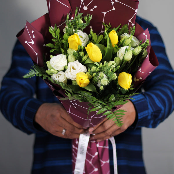 Yellow tulips and white Eustoma with fresh greenery wrapped in burgundy Korean-style flower sheets