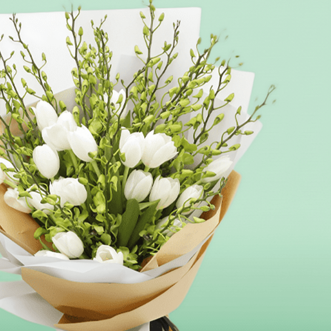 White tulips and orchid stems arranged with greenery in white and natural-toned wrapping
