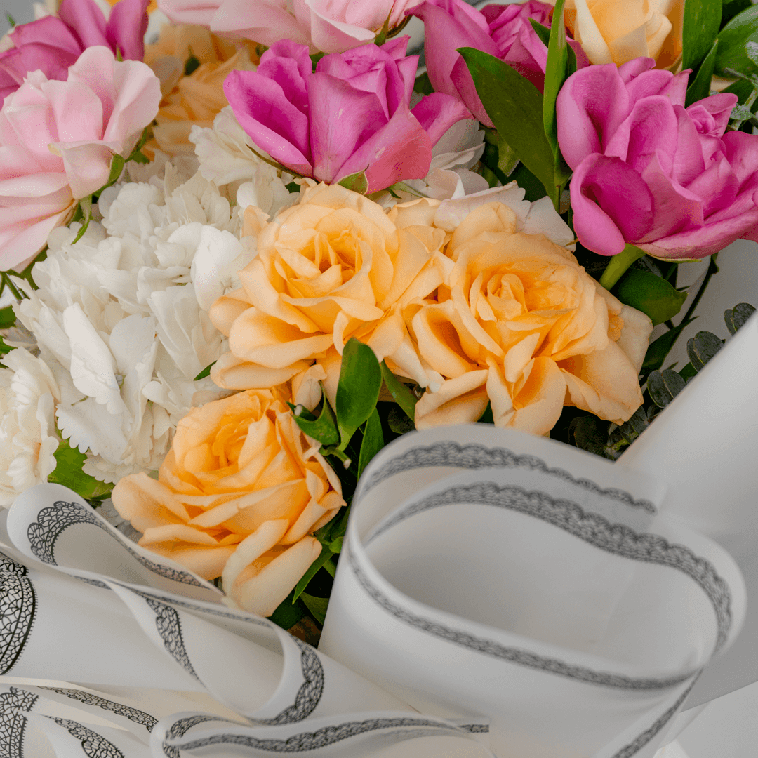 Pastel hand bouquet with pink and peach roses, white lilies, hydrangeas and eucalyptus in elegant grey wrapping.