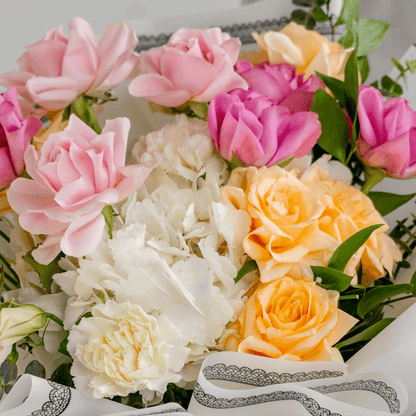 Pastel hand bouquet with pink and peach roses, white lilies, hydrangeas and eucalyptus in elegant grey wrapping.