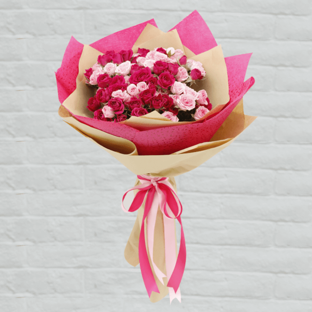 A bouquet featuring red and pink spray roses in pink and kraft-style non-woven wrapping, finished with matching ribbons.
