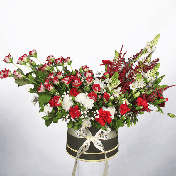 Red spray roses, white carnations, astilbe and fresh greenery arranged in a black round flower box.
