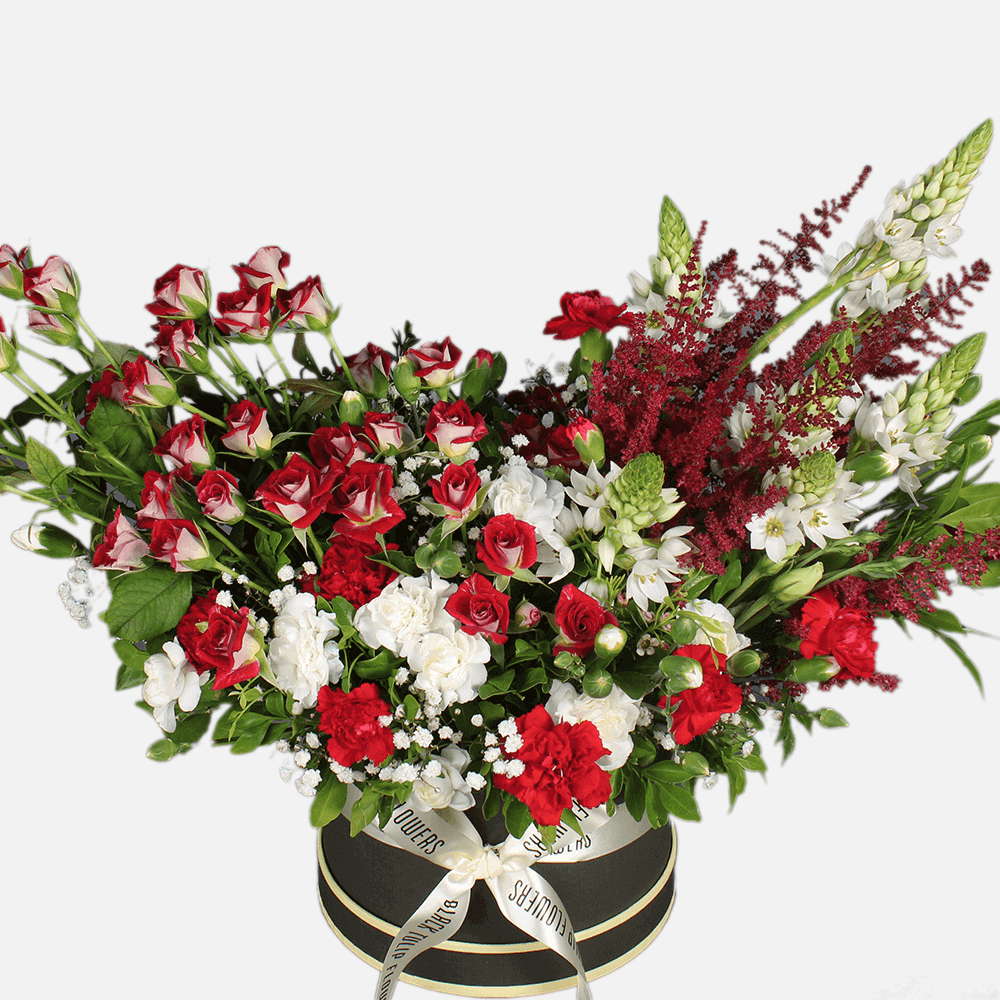 Red spray roses, white carnations, astilbe and fresh greenery arranged in a black round flower box.
