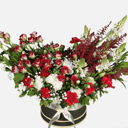 Red spray roses, white carnations, astilbe and fresh greenery arranged in a black round flower box.
