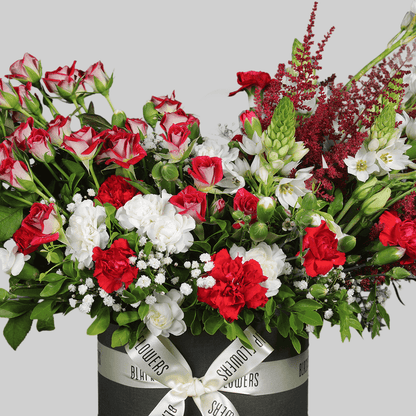Red spray roses, white carnations, astilbe and fresh greenery arranged in a black round flower box.
