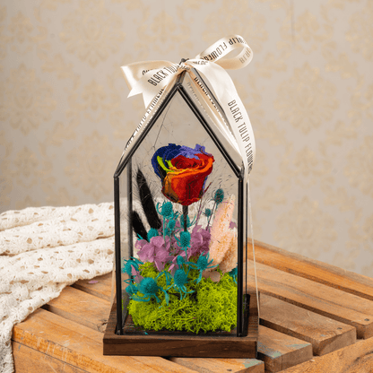 Preserved rainbow roses with dried flowers displayed in a clear glass dome.