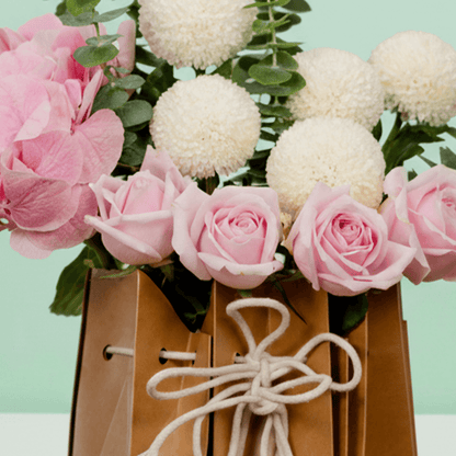 20–25 pink roses with eucalyptus arranged in a decorative cane paper bag.