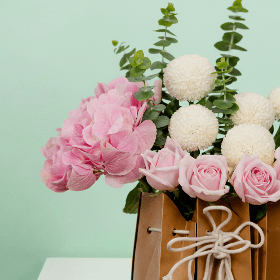 Mixed hydrangeas, roses, ping pong flowers and eucalyptus arranged in a rustic paper bag.