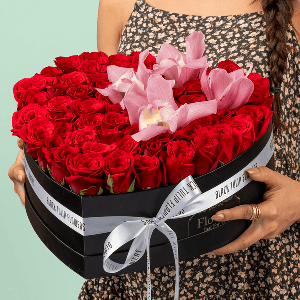 Red roses and pink cymbidium orchids in black heart box