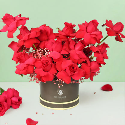20 red Roses with Gypsophila arranged in a round grey flower box.