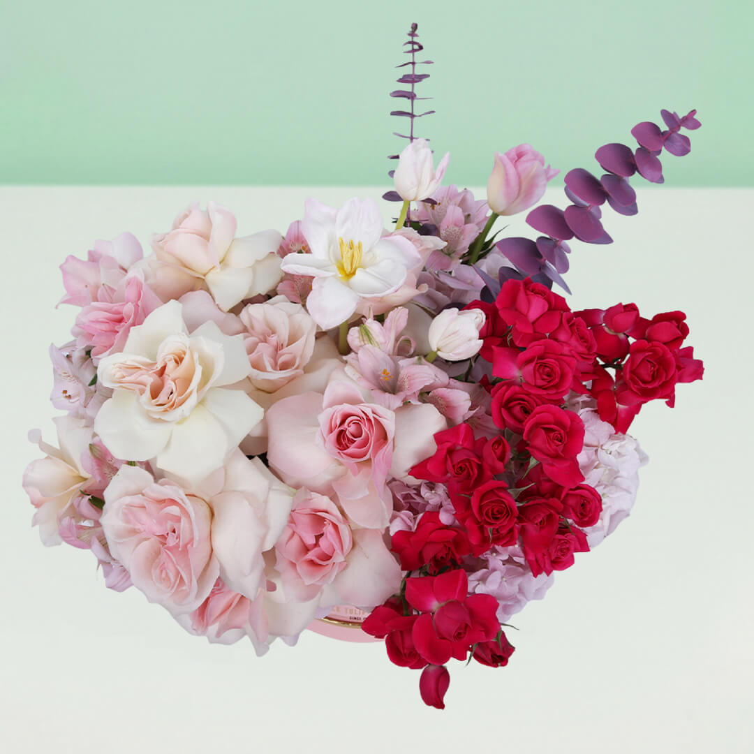 Roses, Spray Roses, Tulips and Hydrangeas with greenery arranged in a pink round flower box.