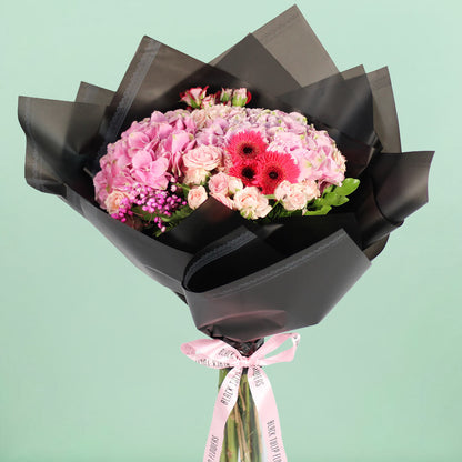 Pink Hydrangeas, Spray Roses, Gerberas and Gypsophila wrapped in black non-woven paper.