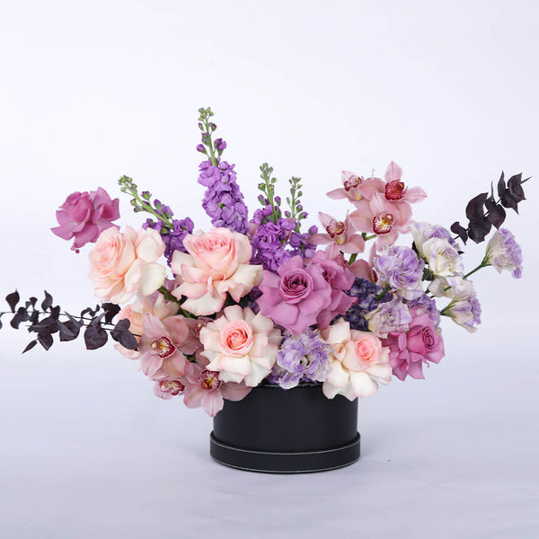 Pastel Roses, Cymbidium orchids, Lisianthus, Hydrangeas and Snapdragons arranged in a black round flower box.