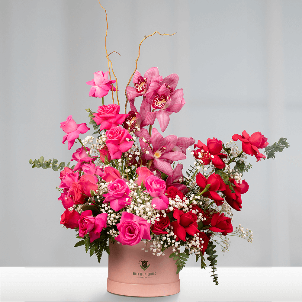 Assorted pink and red Roses with Cymbidium orchids, Gypsophila and Salix Curly branches in a pink round flower box.