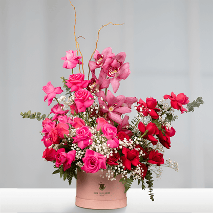 Assorted pink and red Roses with Cymbidium orchids, Gypsophila and Salix Curly branches in a pink round flower box.