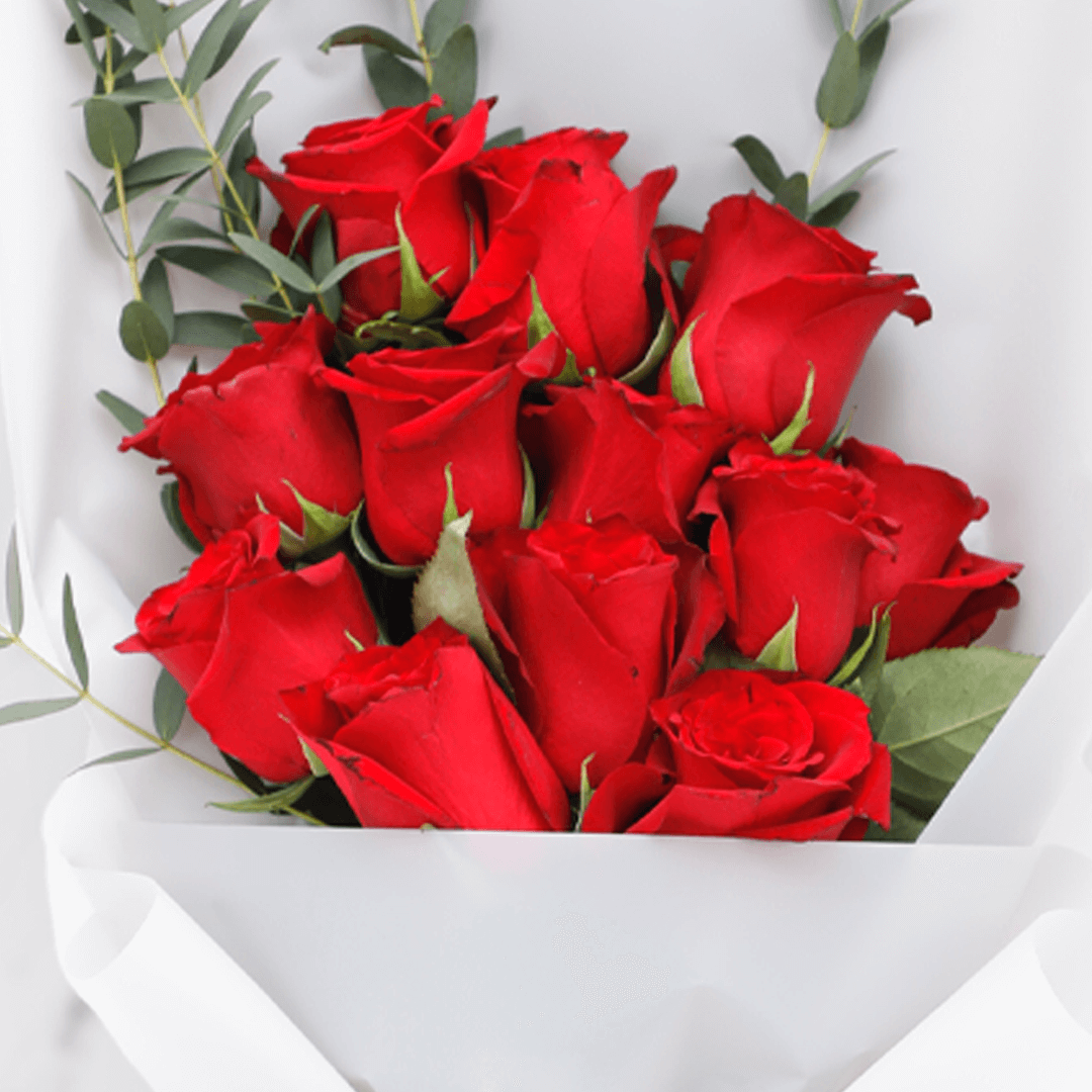 Fresh red roses bouquet with added greenery in a white wrap finished with a red ribbon.