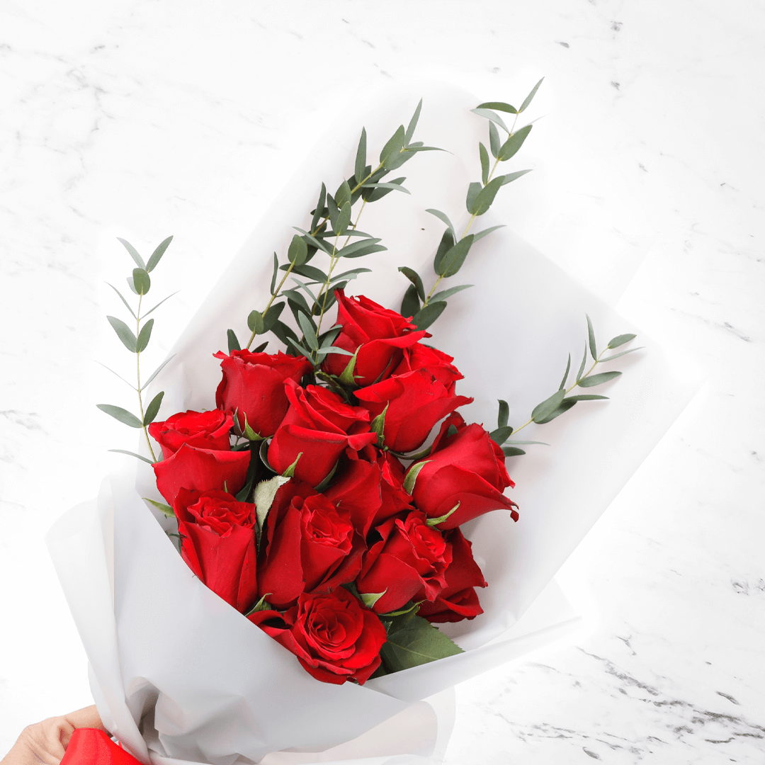 Fresh red roses bouquet with added greenery in a white wrap finished with a red ribbon.