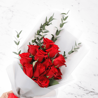 Fresh red roses bouquet with added greenery in a white wrap finished with a red ribbon.