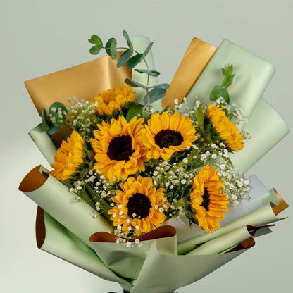 Sunflower bouquet with eucalyptus, white fillers and green wrapping tied with a black ribbon.
