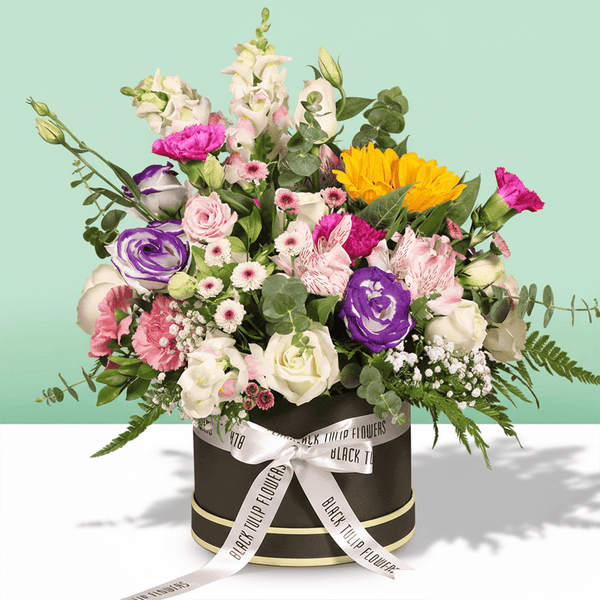 A round flower box arranged with sunflowers, roses, Eustoma, snapdragons, alstroemeria and carnations.