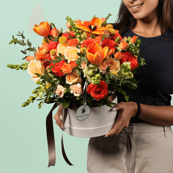 A white flower box filled with orange Tulips, Roses, Snapdragons, Craspedia, Spray Carnations and Eucalyptus.