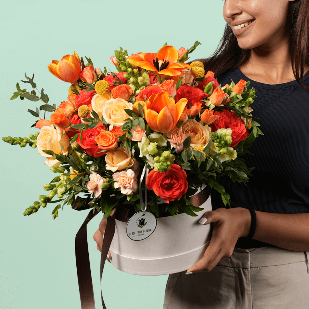 A white flower box filled with orange Tulips, Roses, Snapdragons, Craspedia, Spray Carnations and Eucalyptus.