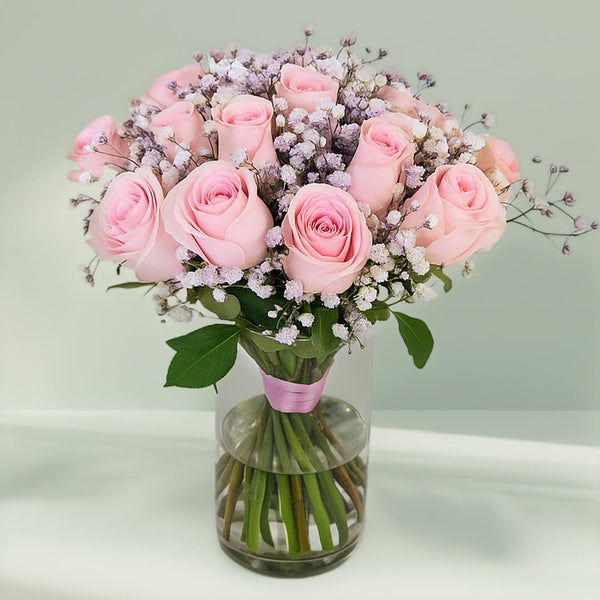 20 pink roses with gypsophila arranged in a clear glass vase.