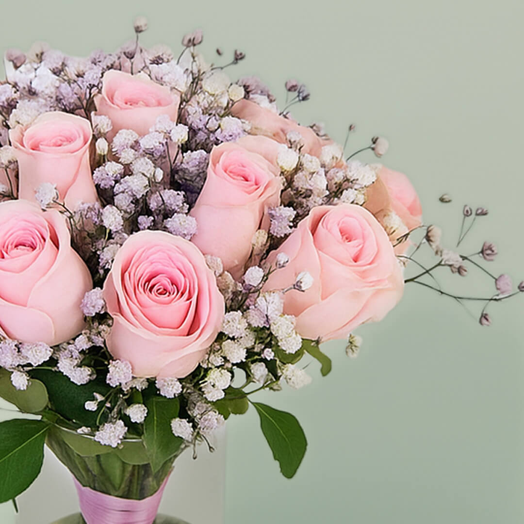 20 pink roses with gypsophila arranged in a clear glass vase.