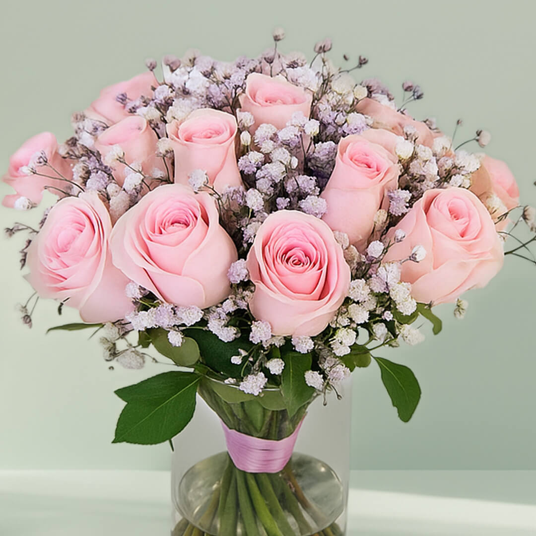 20 pink roses with gypsophila arranged in a clear glass vase.