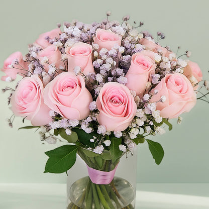 20 pink roses with gypsophila arranged in a clear glass vase.