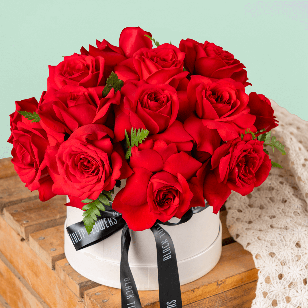 Fresh red roses arranged in a white round flower box with black ribbon