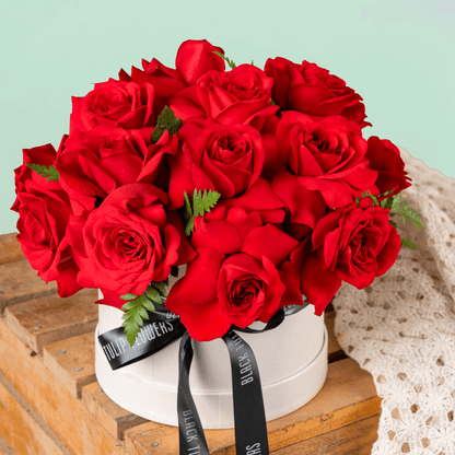 Fresh red roses arranged in a white round flower box with black ribbon