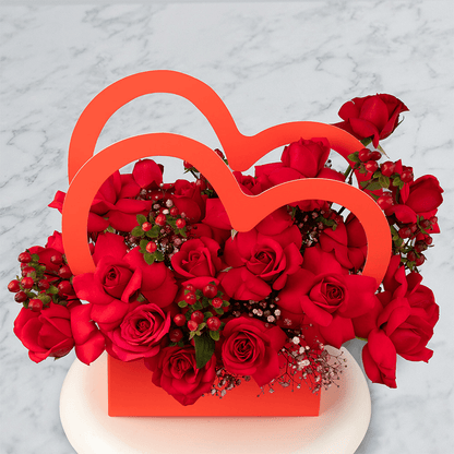 Red Roses with berries and Gypsophila arranged in a red heart-shaped flower box.
