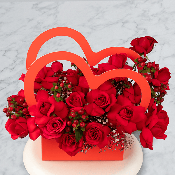 Red Roses with berries and Gypsophila arranged in a red heart-shaped flower box.
