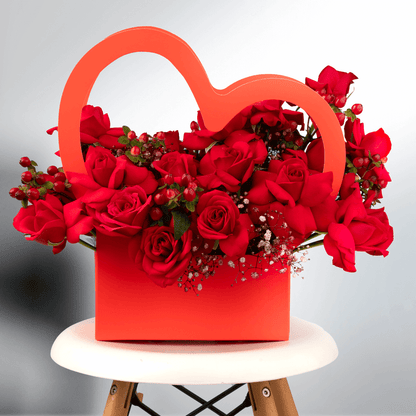 Red Roses with berries and Gypsophila arranged in a red heart-shaped flower box. 