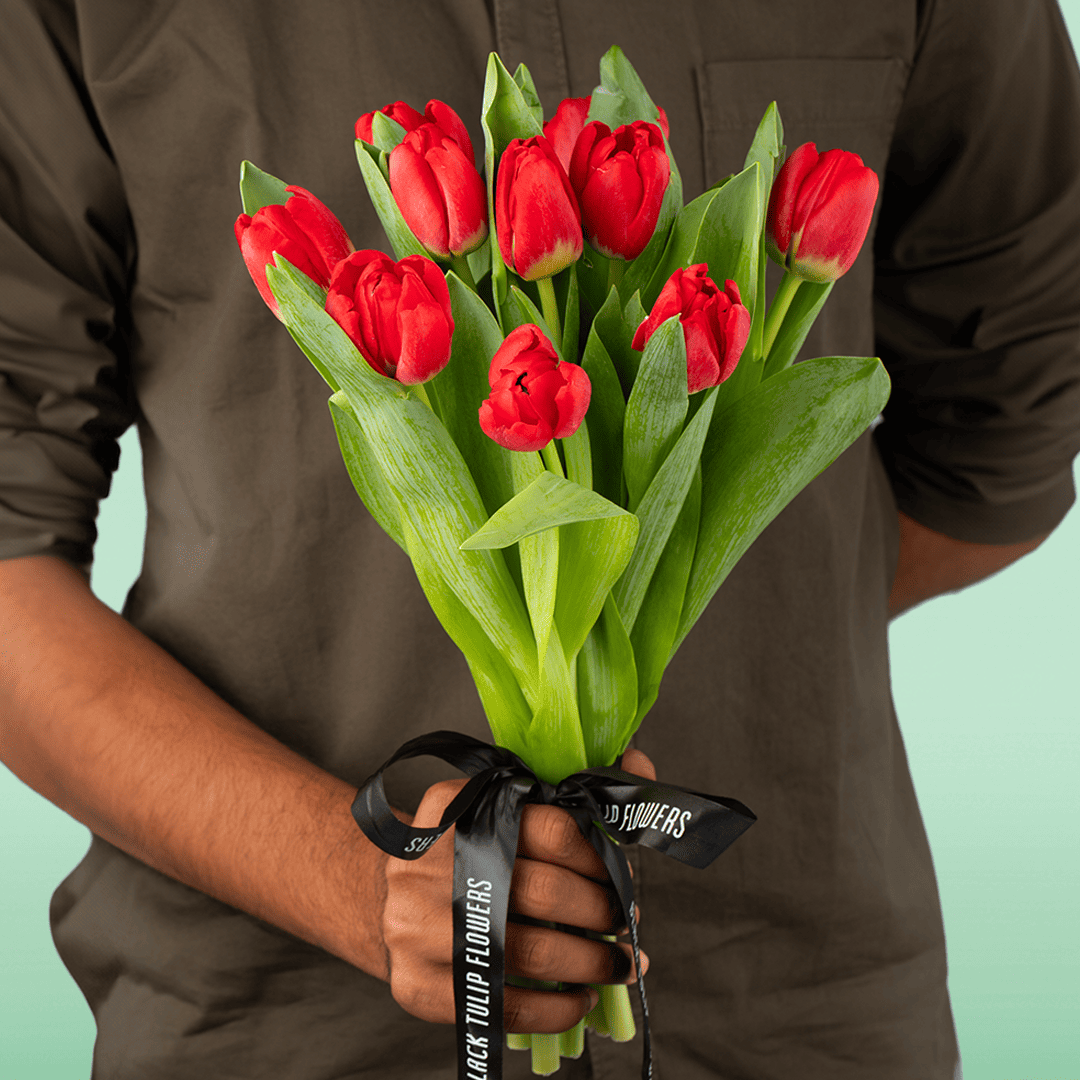 Hand-tied bouquet of 10 fresh red tulips with green foliage and black ribbon.