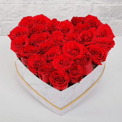 Red roses closely arranged in a small white heart-shaped box with gold rim
