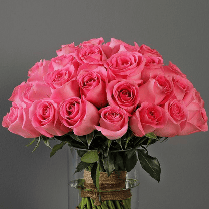 An elegant display of 30 pink roses and fresh greenery presented in a sleek transparent cylinder vase.