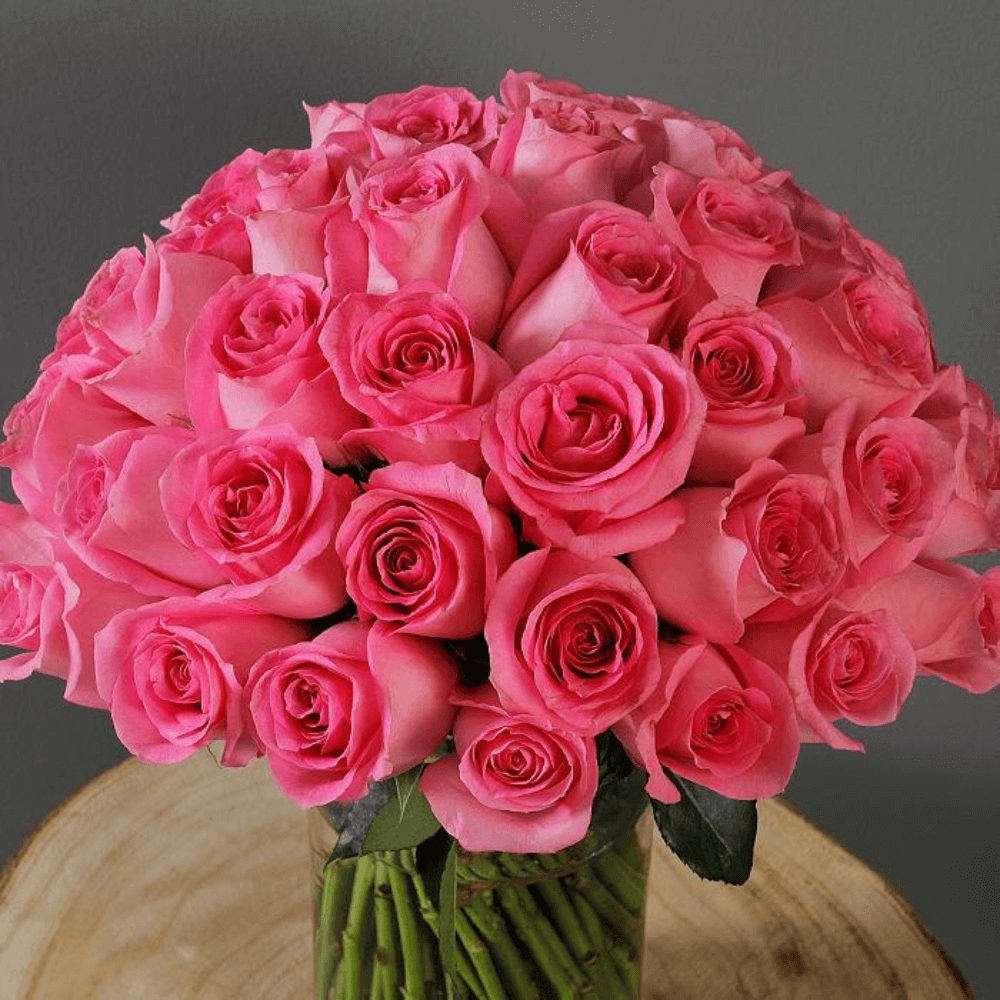 An elegant display of 30 pink roses and fresh greenery presented in a sleek transparent cylinder vase.