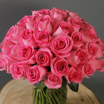 An elegant display of 30 pink roses and fresh greenery presented in a sleek transparent cylinder vase.