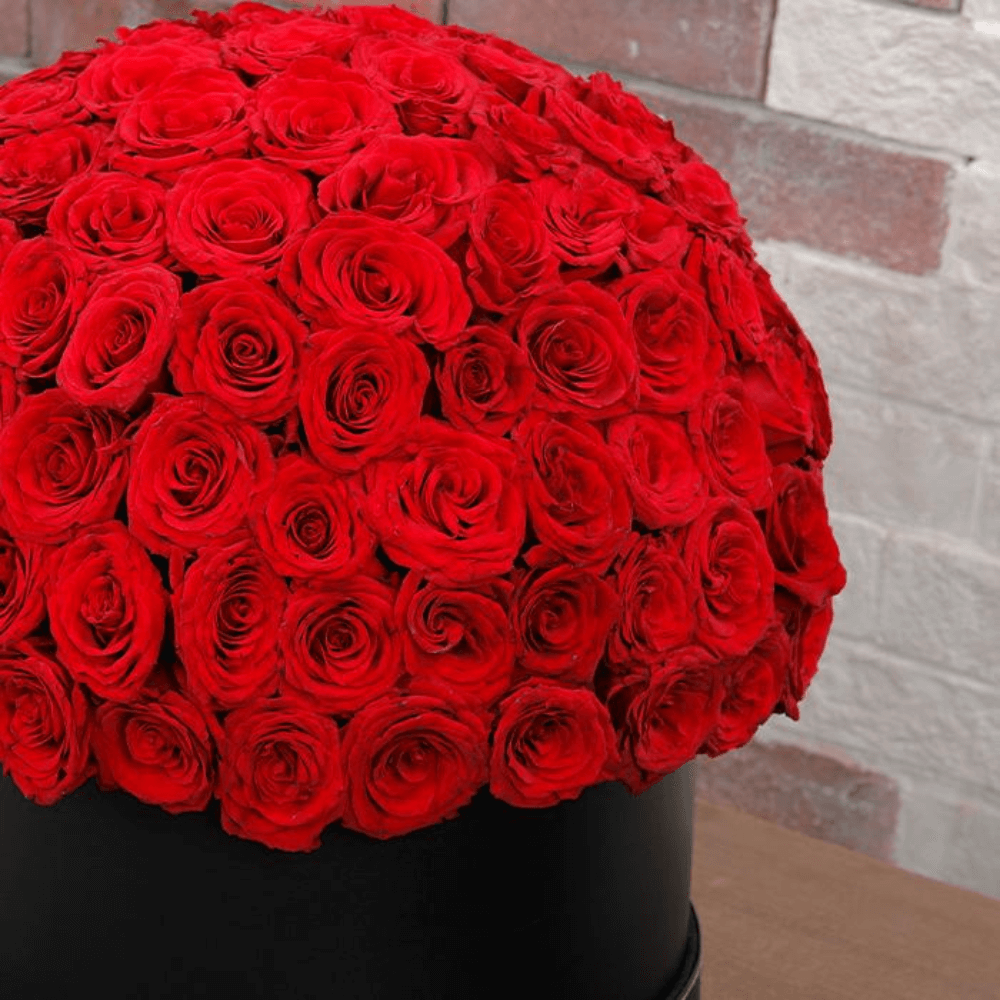Large dome arrangement of red roses displayed in a black round hat box
