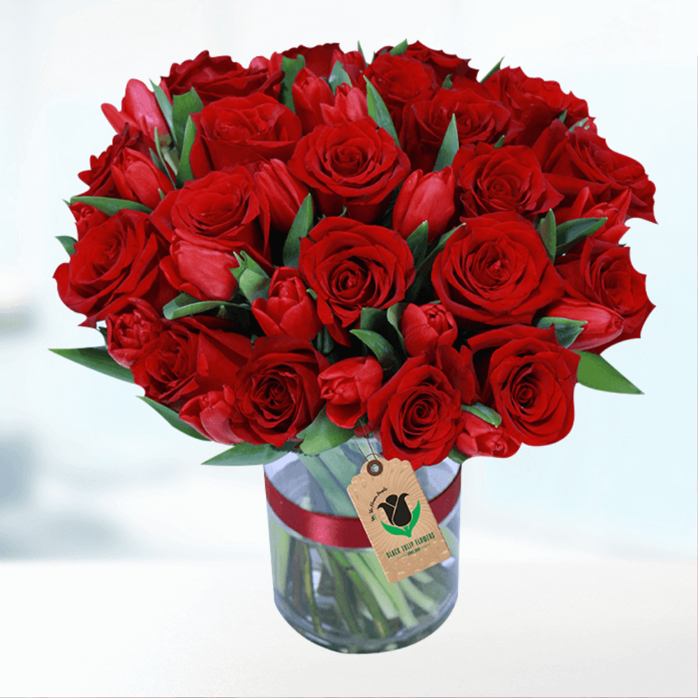 Red roses and tulips arranged in a transparent cylindrical glass vase