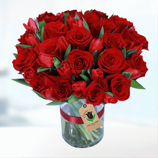 Red roses and tulips arranged in a transparent cylindrical glass vase