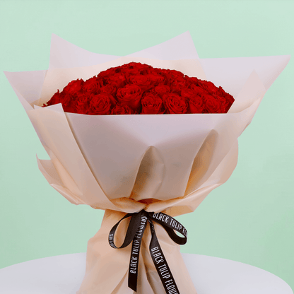 Fresh Hand-tied bouquet of 50 red roses elegantly wrapped and tied with a black ribbon.