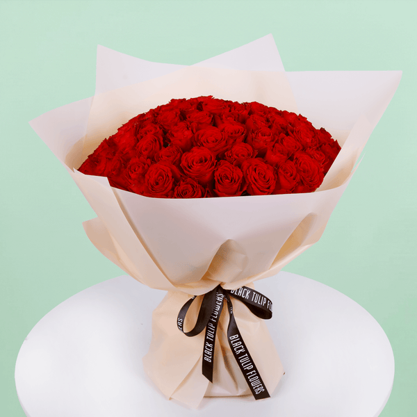 Fresh Hand-tied bouquet of 50 red roses elegantly wrapped and tied with a black ribbon.